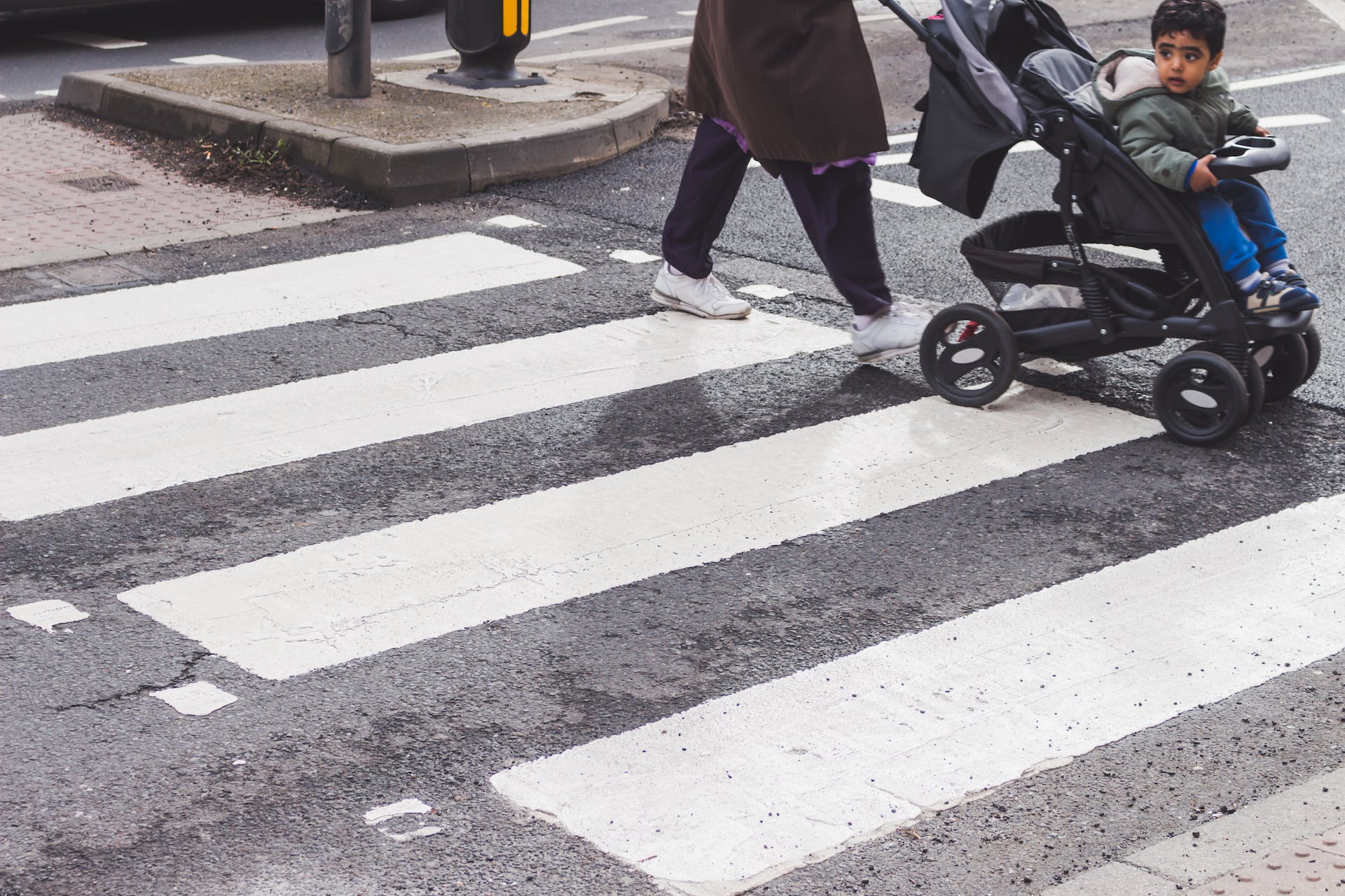 An individual pushes a stroller, with a toddler inside, as they cross the bustling city street, both taking in the urban scenery.
