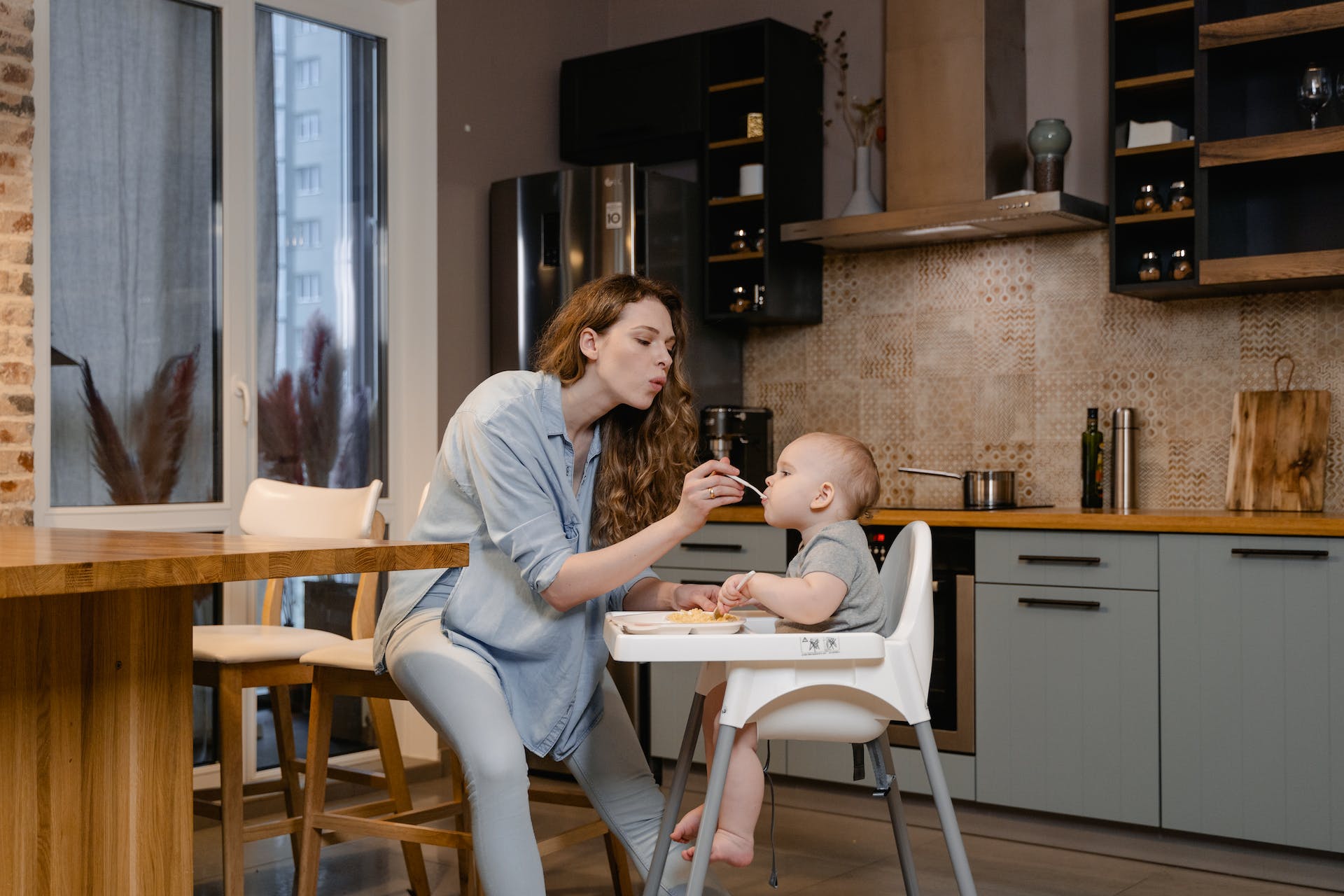 A woman feeds a baby sitting in a high chair, with a spoon.