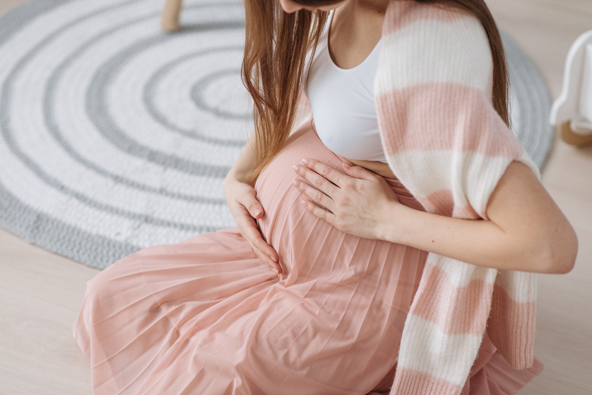 Pregnant woman sits on floor and holds her belly
