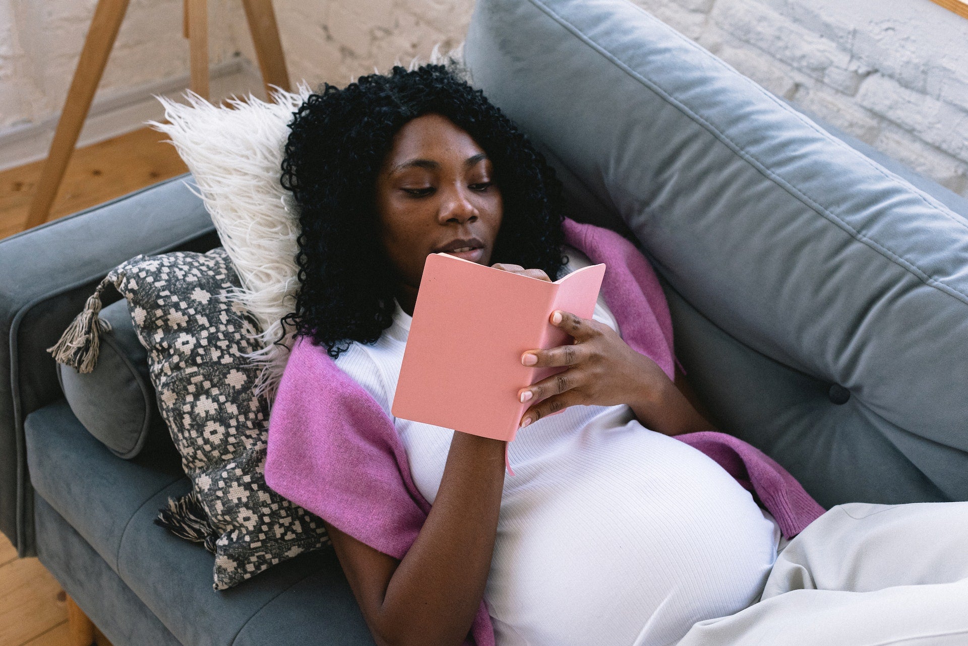 Pregnant woman lays on couch writing in a journal