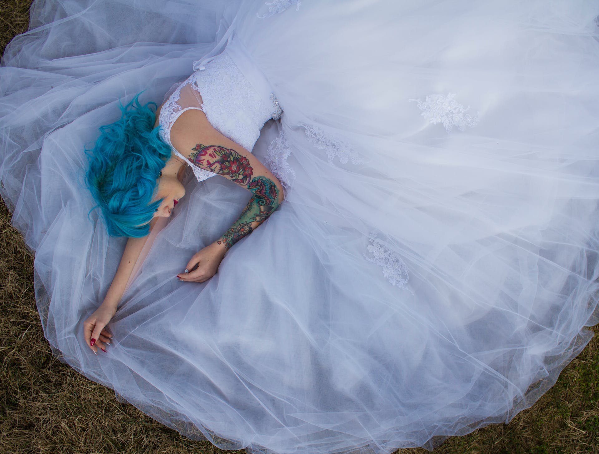 A tattooed woman in a white gown lays on the grass