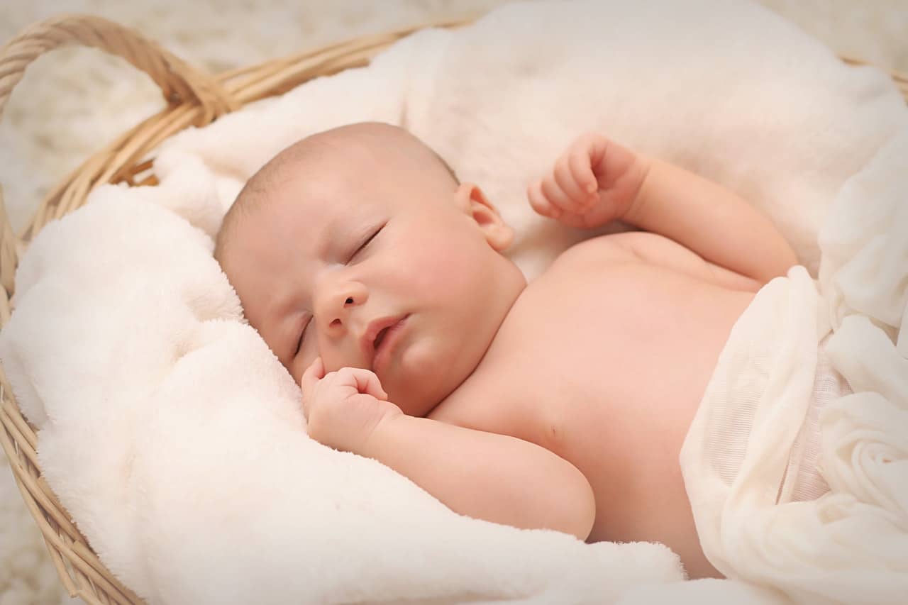 a baby sleeping on a white blanket in a basket