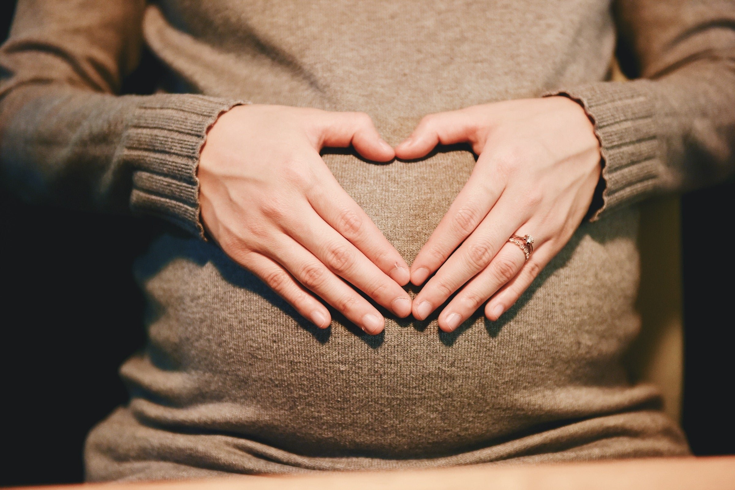Pregnant woman making heart sign on stomach