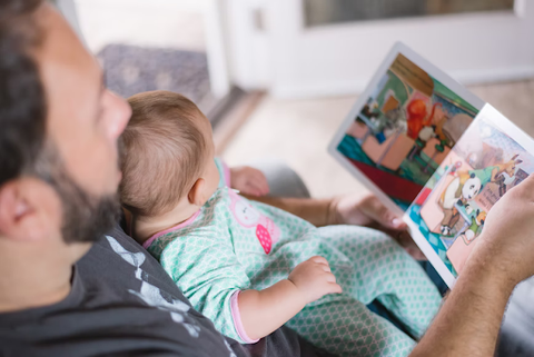 Father with baby in his lap as he reads the baby a picture book.