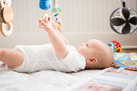 A small baby lying on a mat and playing with sensory toys hanging over it.