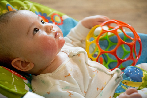 Cute baby sitting in a basket with a ball-like toy nearby and looking upwards.