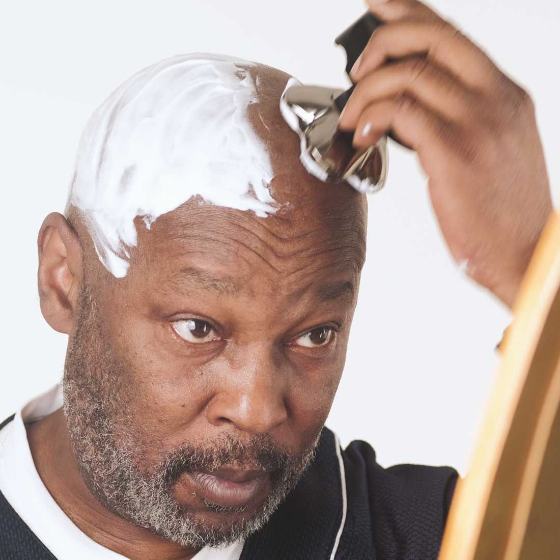 A bald guy with shaving foam on his head shaving with skull shaver. The Carver PRO 4 head blades can shave wet or dry