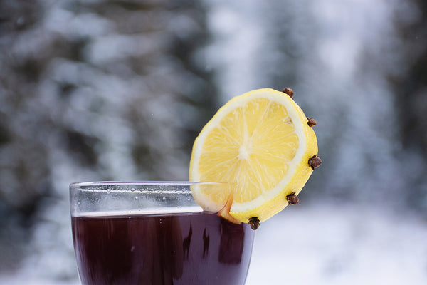 dark colored drink garnished with clove-studded lemon wheel against a snowy background