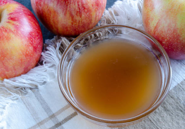 cup of raw apple cider vinegar on a plaid dishtowel with whole red apples nearby