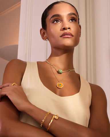 A model wears two layered necklaces with green and gold pendants