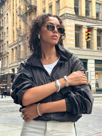 A model stands with her arms crossed wearing three silver bracelets and silver earrings