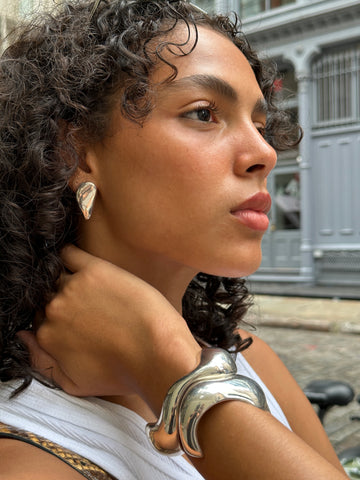 A model wears silver earrings and two silver cuff bracelets by AGMES