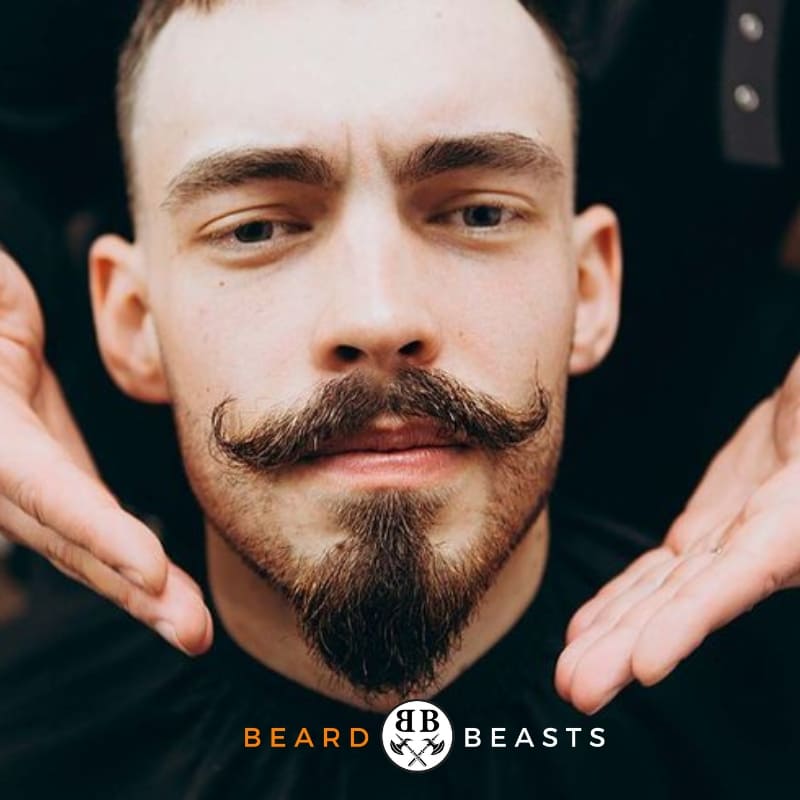 Confident young man with a sculpted anchor beard style and curled mustache, showcasing modern facial hair trends by Beard Beasts.