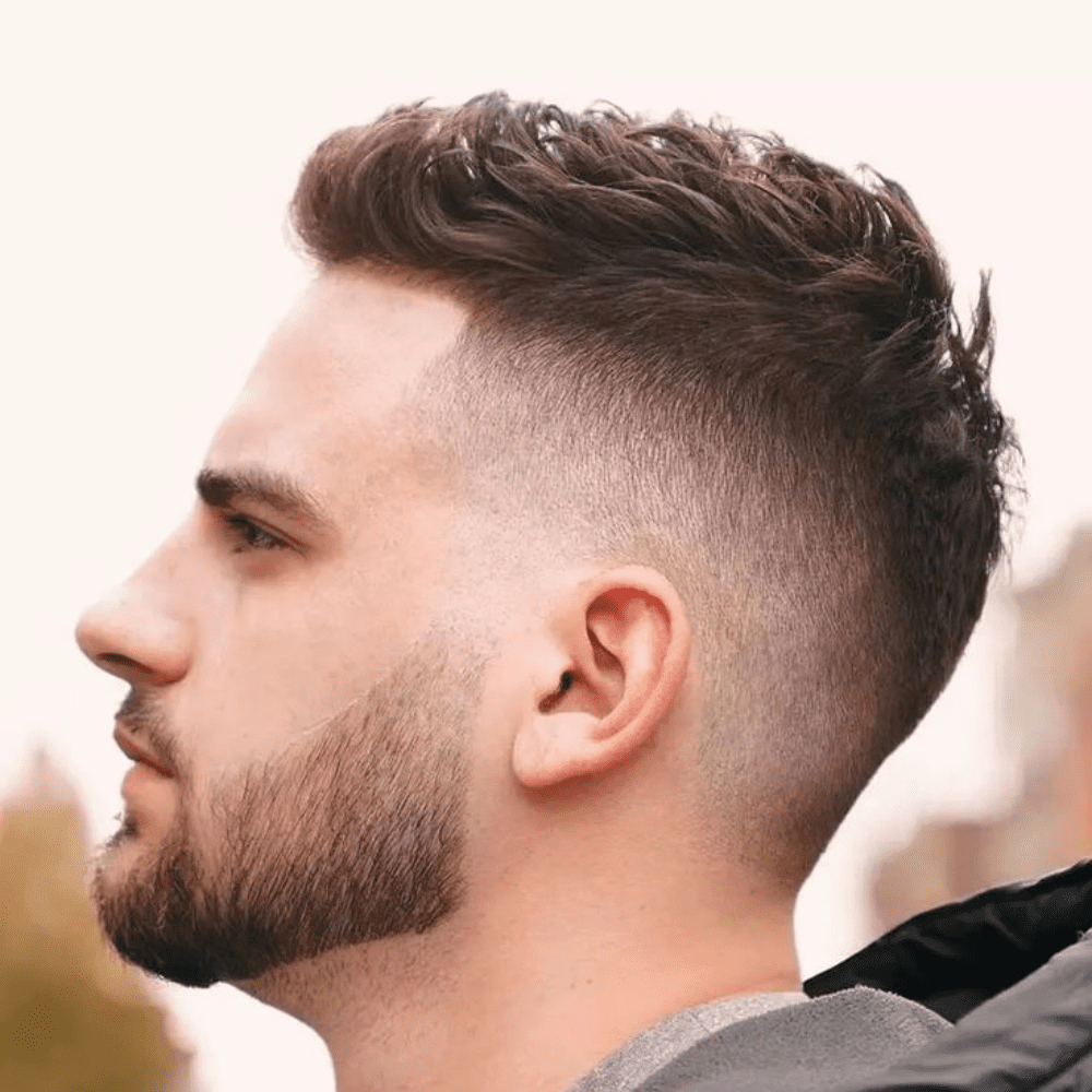 Profile view of a young man sporting a modern textured quiff with a neatly tapered fade, showcasing a popular pomade hairstyle for men.