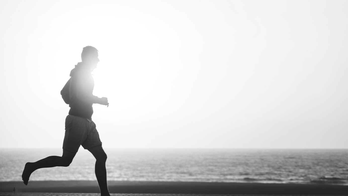 Silhouette of a man jogging at sunrise on the beach, embodying an active morning routine for men