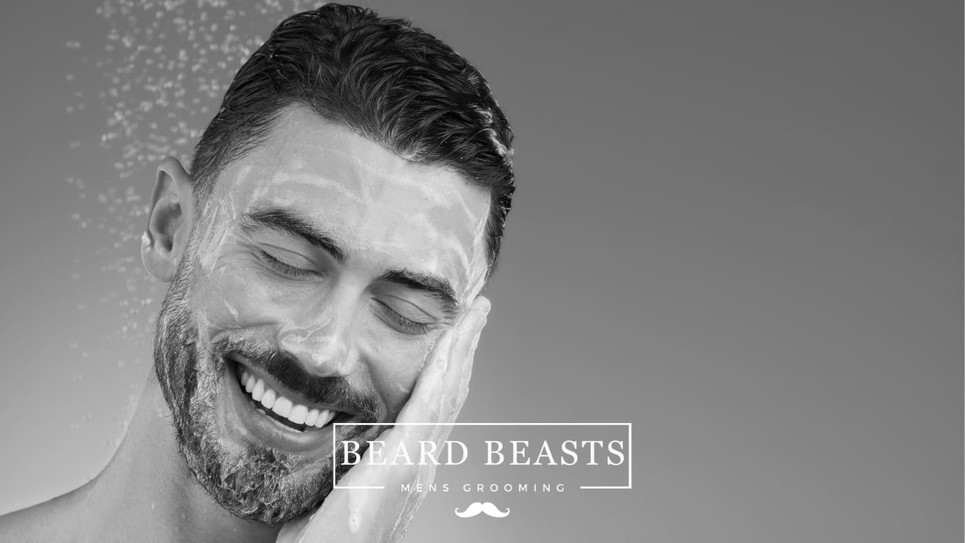 A smiling man with a beard applies cleanser to his face, demonstrating a step in a skincare routine on how to get clear skin for men.