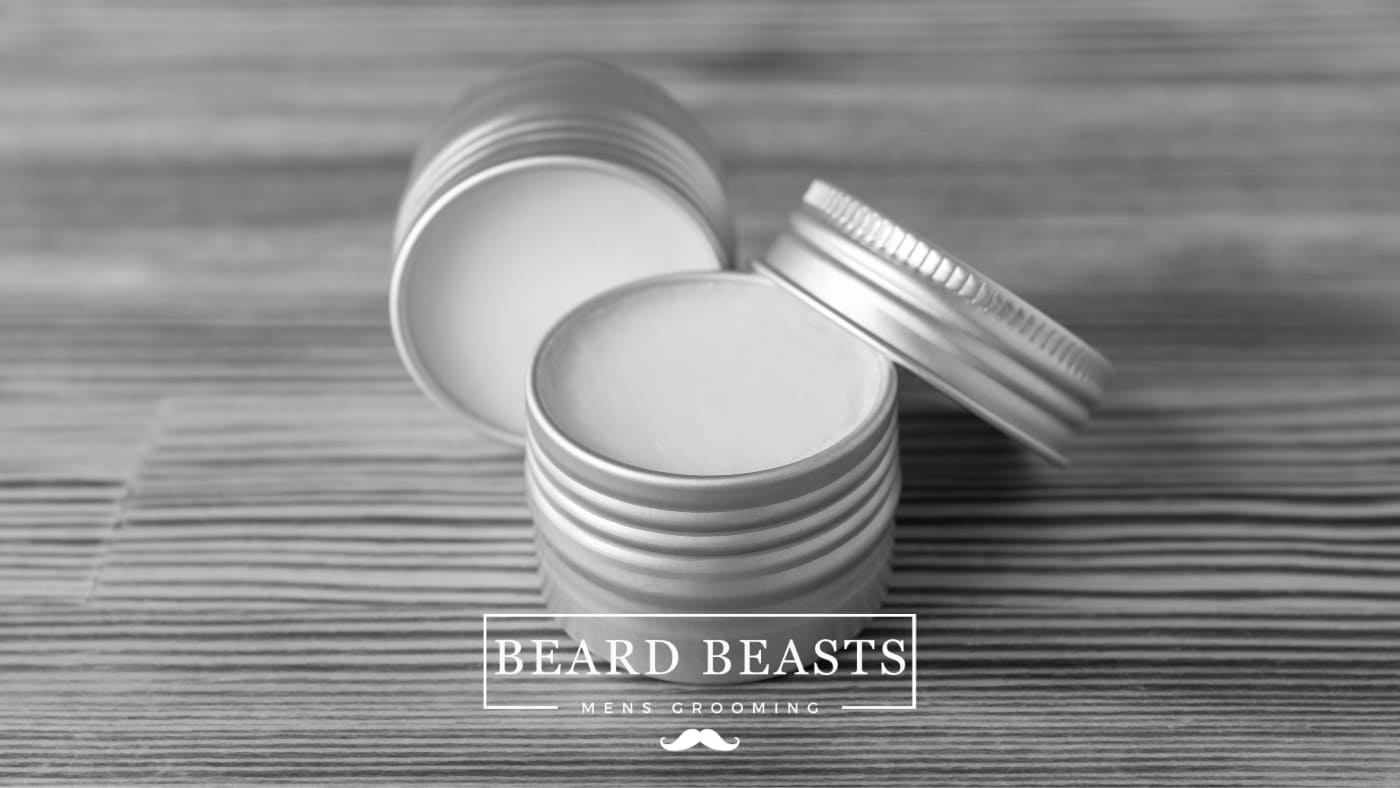 Beard balm in an open tin showcasing its texture, on a wooden surface, with Beard Beasts Men's Grooming logo, demonstrating what does beard balm do for your beard.