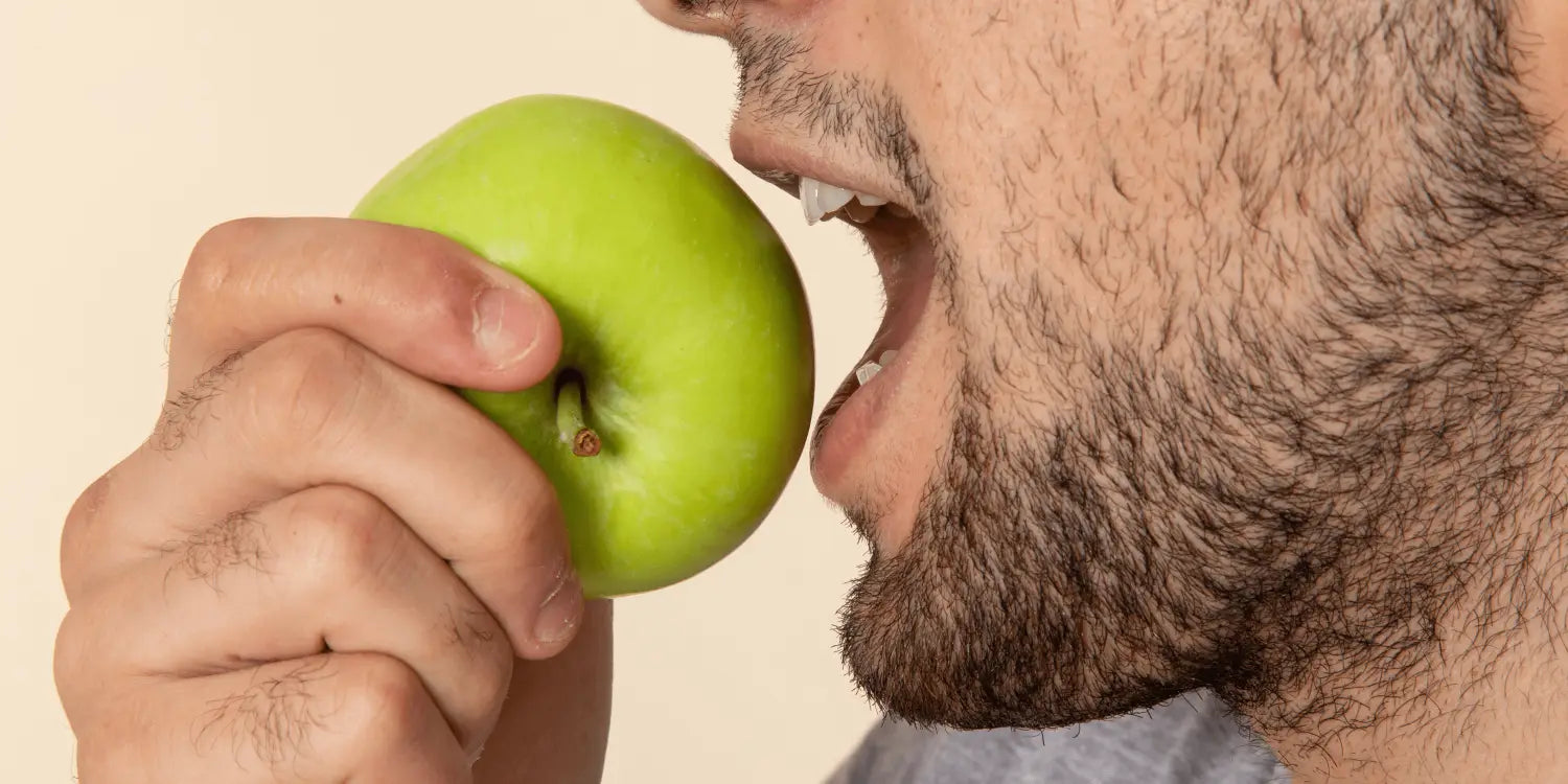 Bearded man enjoying a crisp, juicy apple as part of a healthy diet for promoting full, lush beard growth.