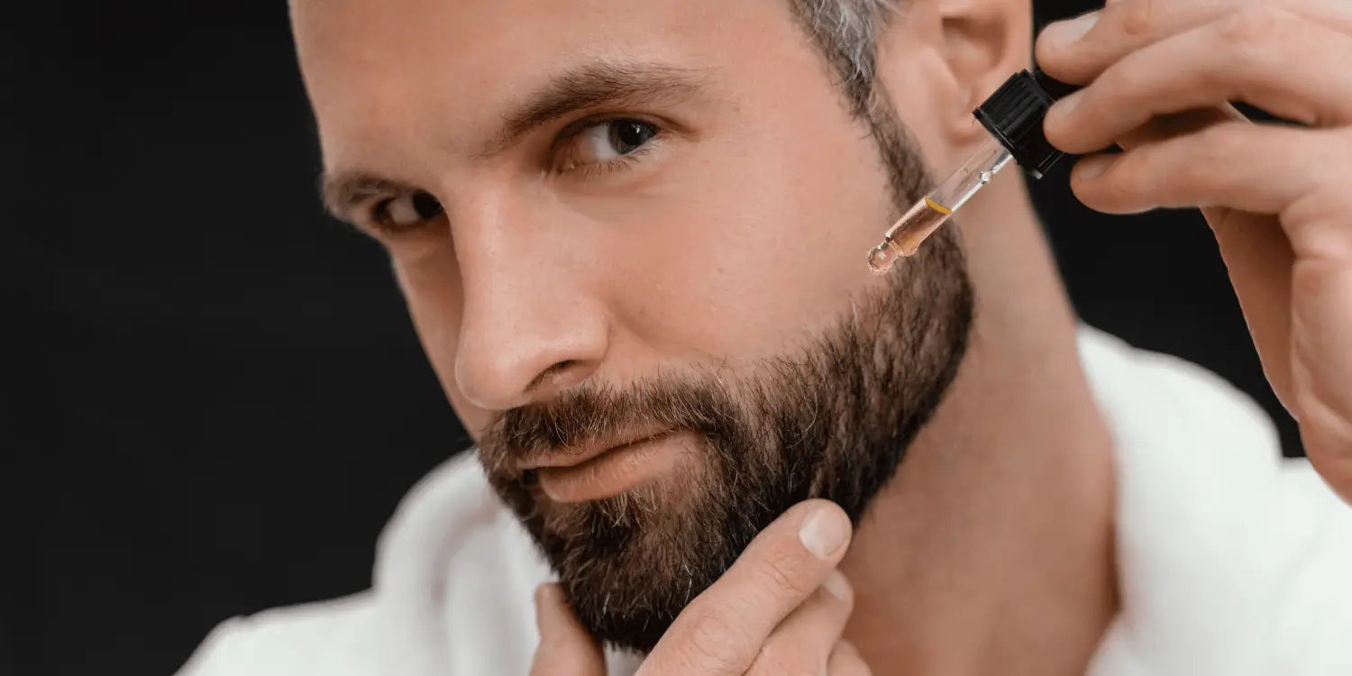 A bearded man meticulously applying beard oil, reflected in a mirror, to soothe and nourish his facial hair, in his journey to combat the itchy beard phase.