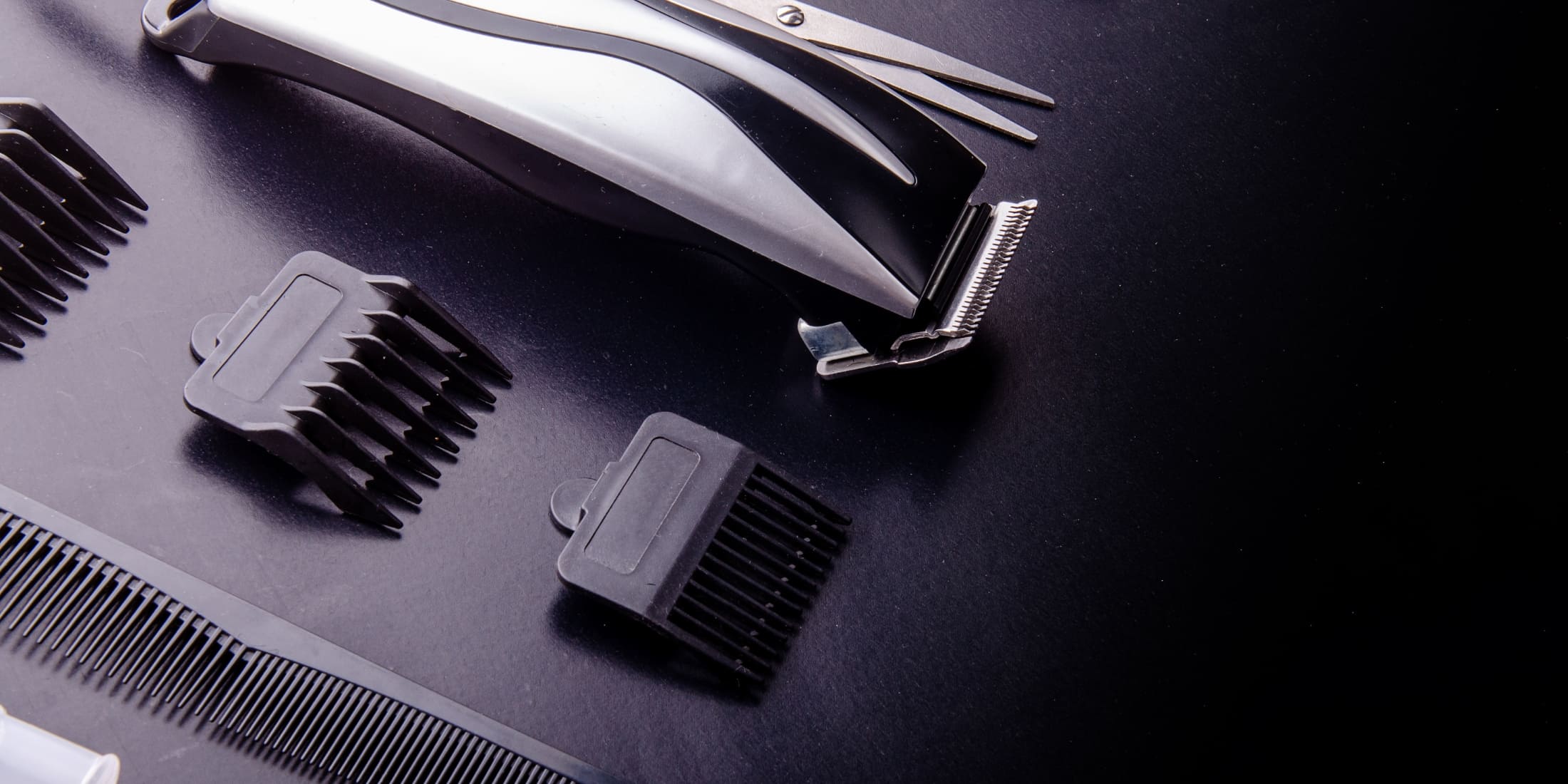 Silver hair clipper with detachable guards and a fine-toothed comb laid out on a black background.