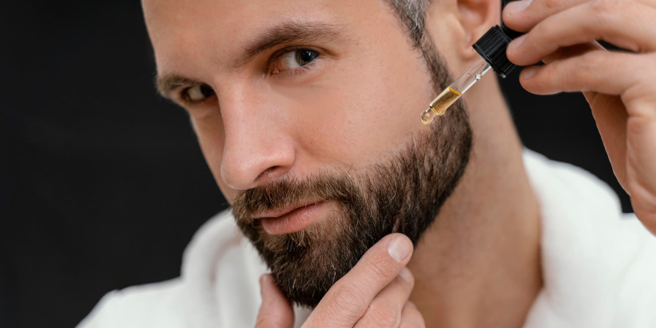 A close-up of a man with a styled beard applying beard oil with a dropper, demonstrating the routine of how often you should apply beard oil for maintaining beard health and style.