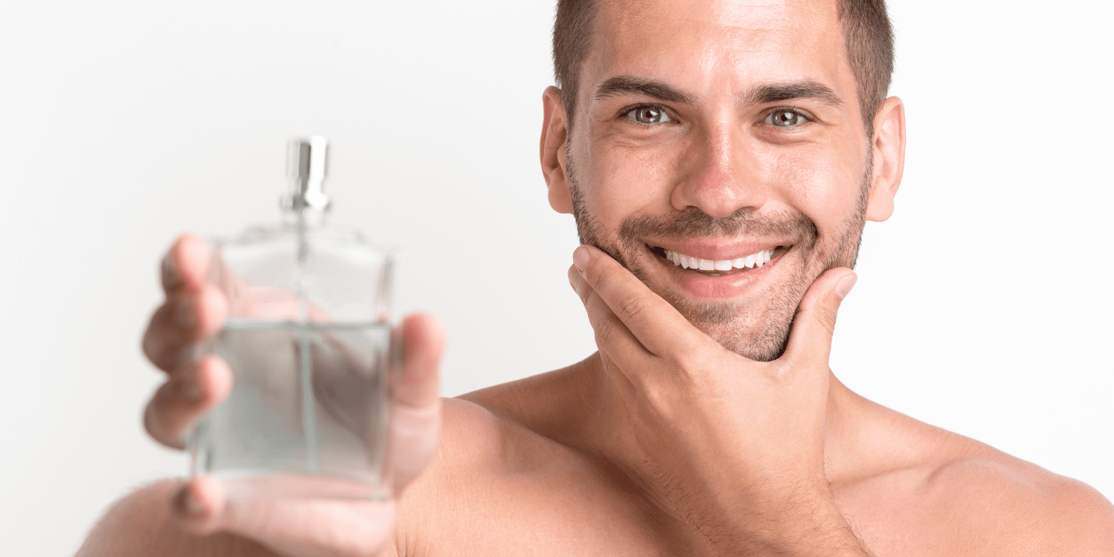 Smiling man holding a bottle of cologne in one hand while touching his freshly shaven face with the other. The image highlights a clean, smooth complexion, emphasizing the use of aftershave and cologne in a grooming routine.