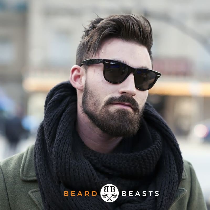 Man with one of the ideal beard styles for a round face, the short boxed beard wearing sunglasses and a chunky knit scarf, with a logo for Beard Beasts on the image