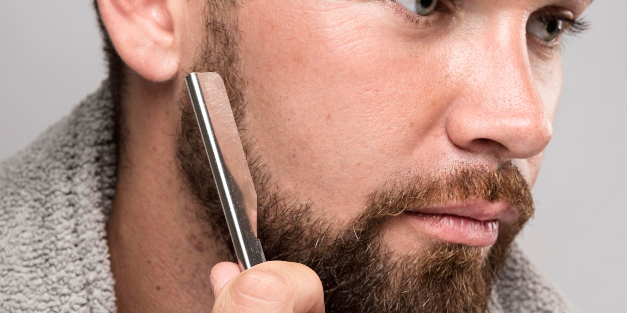 Close-up of a man using a straight razor to shave his beard, highlighting the precision and closeness of shave in the straight razor vs safety razor comparison.