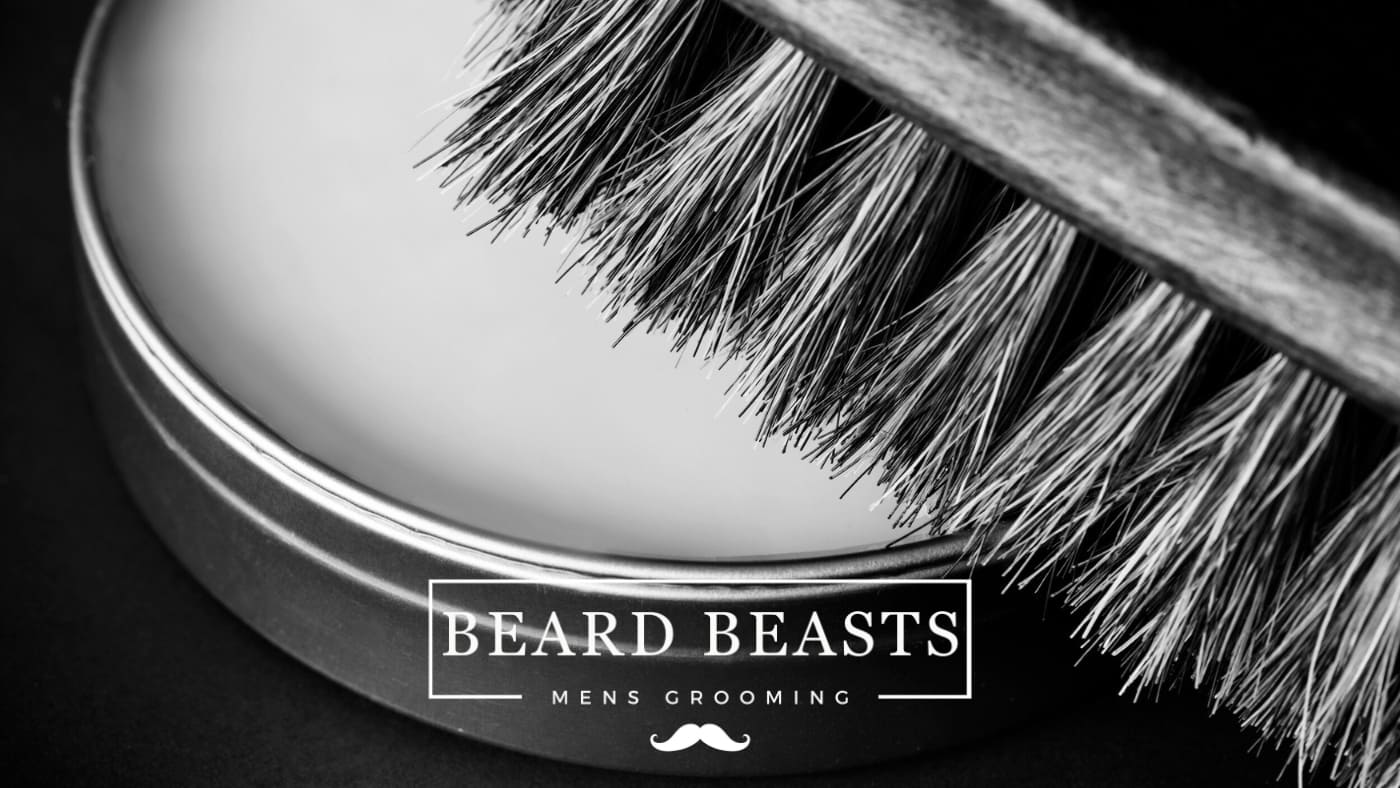 An elegant black and white close-up of a tin of beard balm from Beard Beasts Men's Grooming, with a brush whose bristles are in focus, showcasing the texture and potential use of the balm for beard care. The image is styled to represent high-quality grooming essentials, aimed at those seeking guidance on how to use beard balm for maintaining a polished beard.