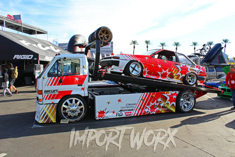 The Baller Hauler is a customized Isuzu NPR box truck that has been transformed to haul a 1986 Toyota Corolla AE86. The Corolla has been modified with a 3S-GE BEAMS engine and Alteeza gearbox, as well as steel aero components. The Isuzu has been updated with an LS-based Vortec 6000 V8 engine, air bag suspension, and a custom hydraulically operated tilt deck with remote winch. Both vehicles have been customized with hand-made fender flares and other custom-fabricated bits. The owner, Miles Shinneman, is a fabricator and has a passion for customizing his rides.