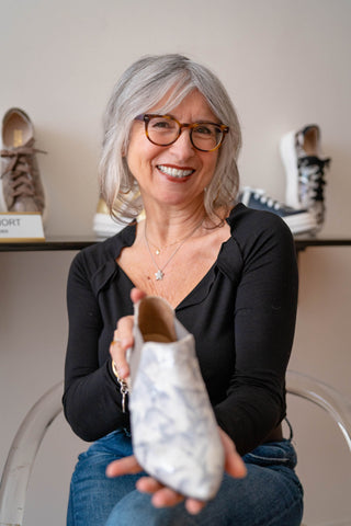 Elena holding one of her designs a silver and white pointed boot
