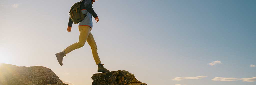 Man jumping across rocks wearing Blundstone boots