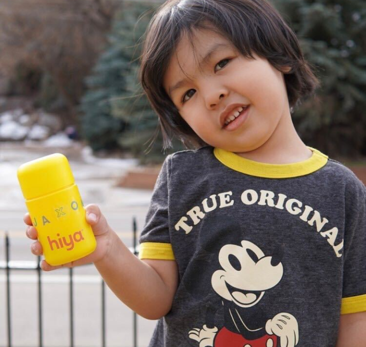 A young boy is holding a bottle of Hiya Kids Daily Multivitamin decorated with stickers.
