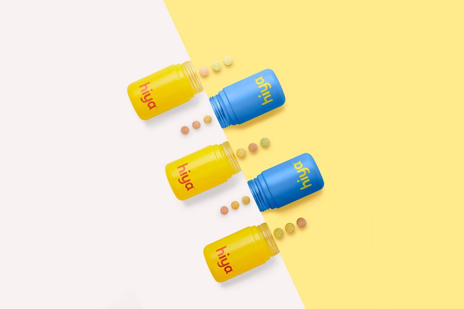 Three yellow Hiya Kids Daily Multivitamin bottles and two blue Hiya Kids Bedtime Essentials bottles open and face each other, with chewable vitamins in front of them.