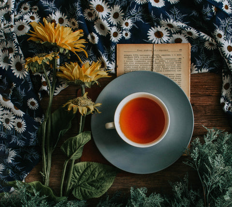 A cup of tea and a book on a table next to some flowers