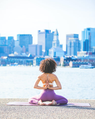 Woman doing yoga by the water with city skyscrapers in the backdrop