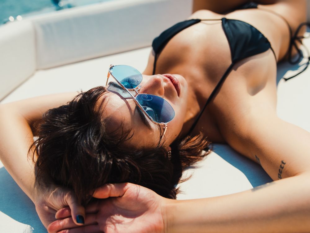 Woman wearing a black bikini and blue sunglasses on a boat