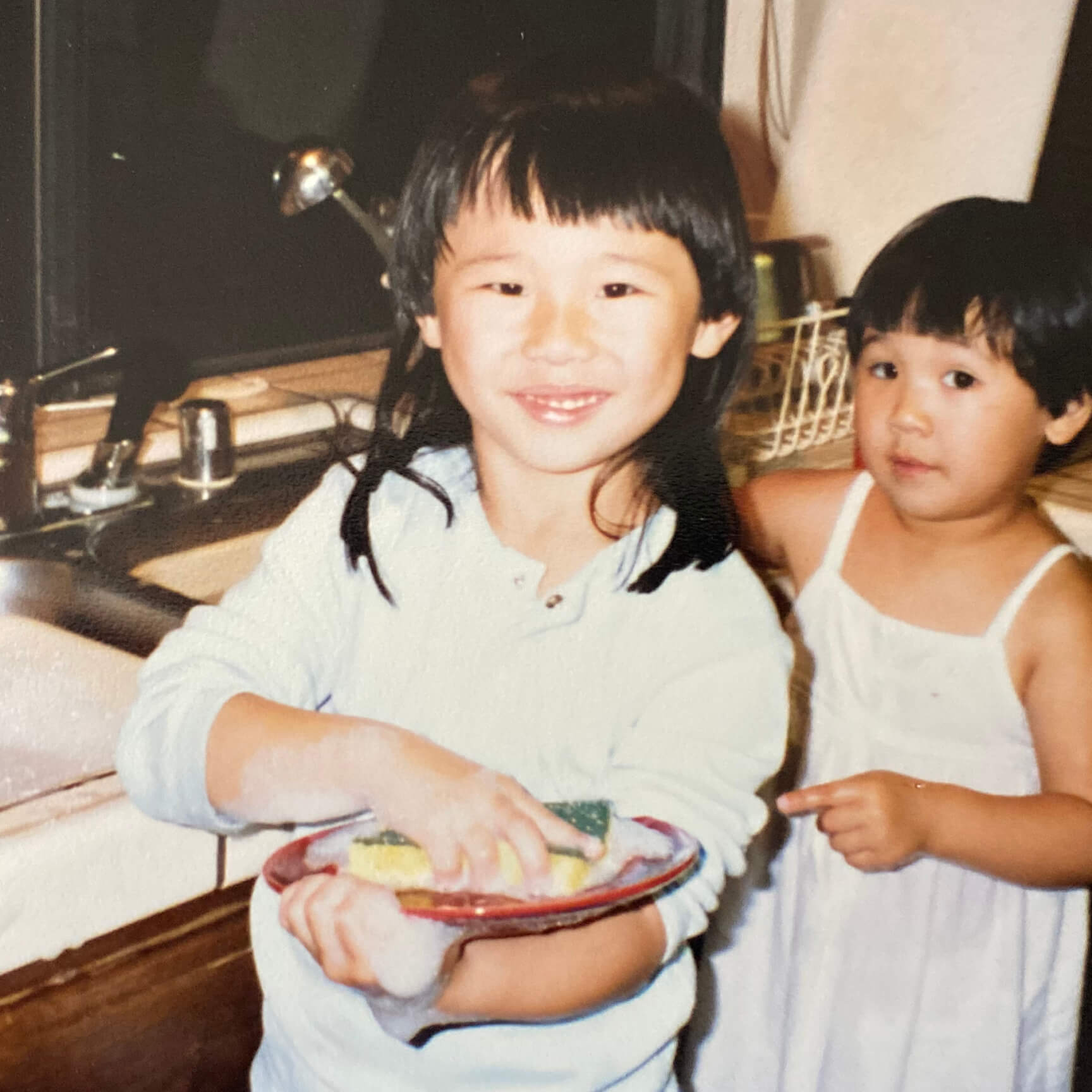 Early childhood photo of Trisha and sister cleaning dishes
