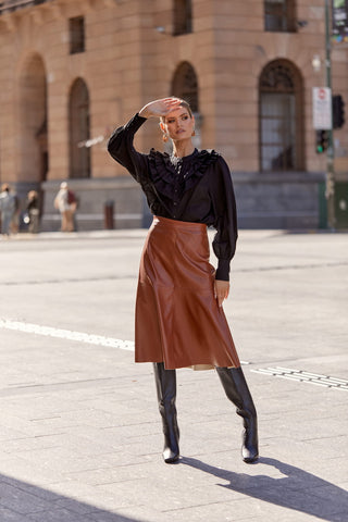 Woman wearing black top and brown faux leather midi skirt in the city
