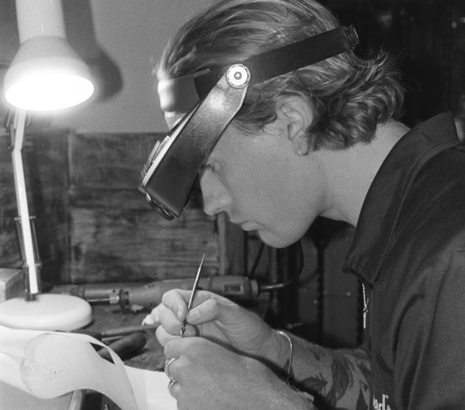 Image depicts jeweller wearing magnifying glasses while creating silver rings.