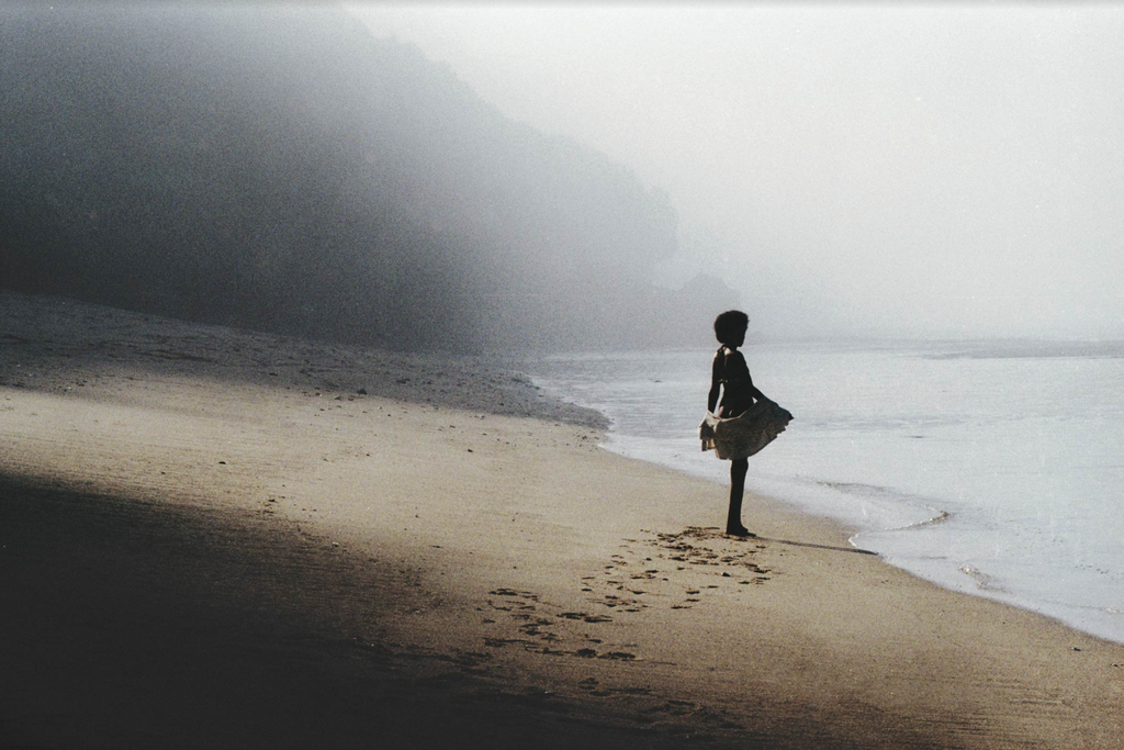 Image depicts woman walking into the distance of a mountainous beach in Bali, Indonesia.