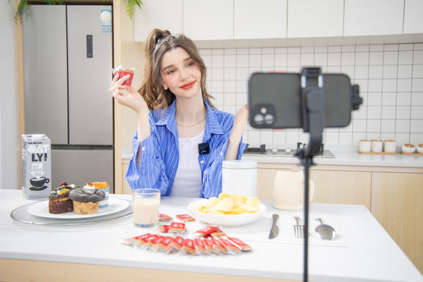 A woman wearing a SVANTTO wireless lavalier microphone is holding food at the table for a LIVE broadcast.