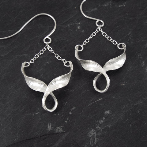 Silver drop earrings with a twisted chevron linked by a loop at the bottom, suspended from the wire by a length of chain.