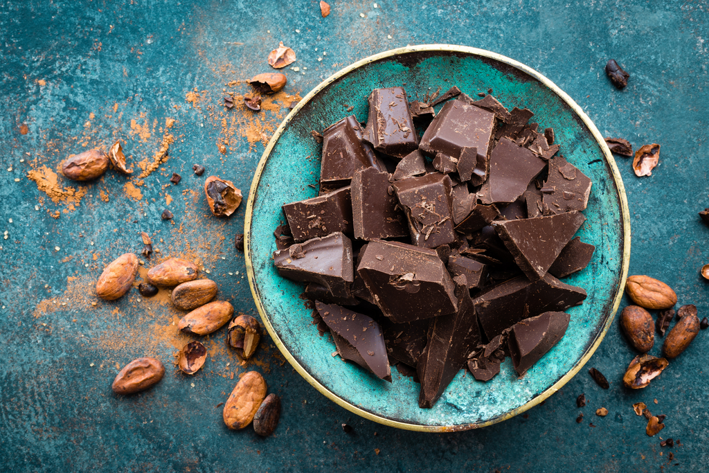 Blue bowl and table with broken pieces of dark chocolate scattered inside and outside