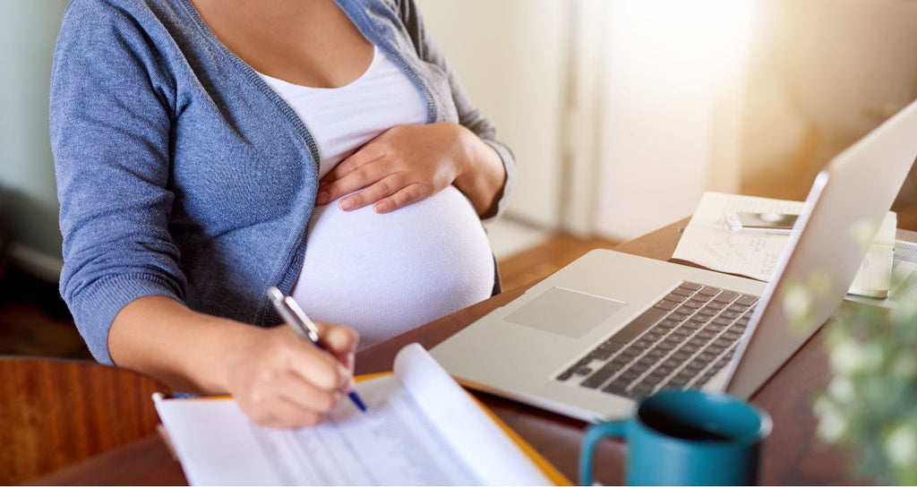 Pregnant woman researching baby furniture on her laptop while making notes. 