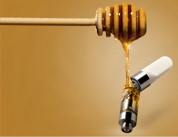 Image of CBD oil poured into a vape cartridge using a wooden honey dripper