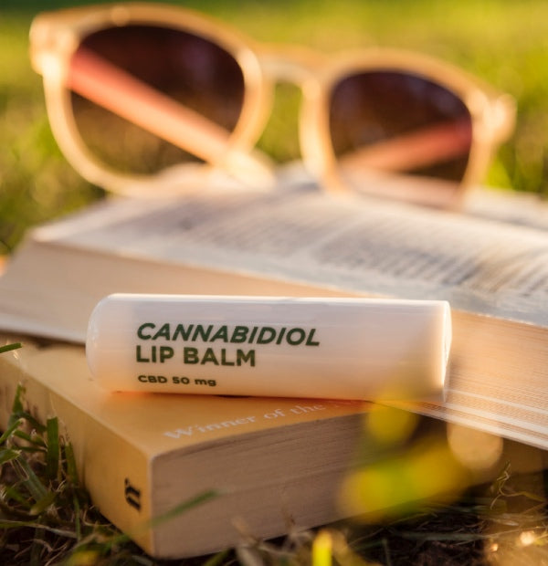 Image of Cannabidiol infused lip balm sitting on books with sunglasses in the background