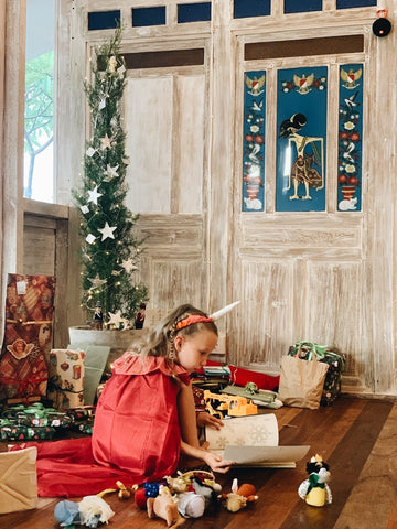 Girl squatting among presents next to Christmas tree