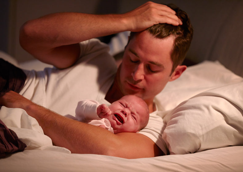 father lying in bed with crying baby daughter