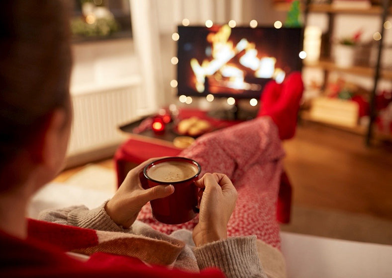 young woman watching tv and drinking coffee with her feet on table at home.